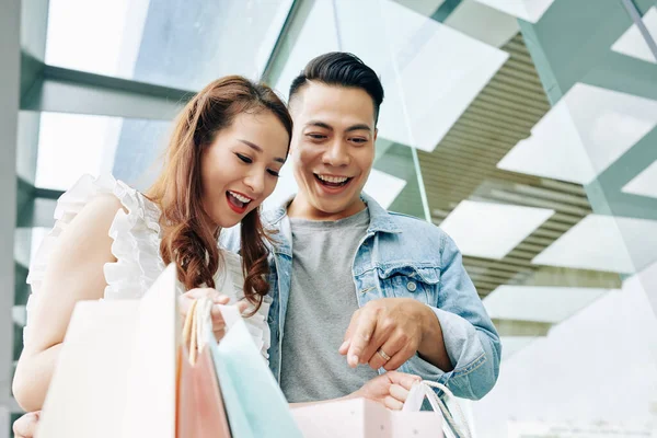 Neşeli genç adam ve kadın alışveriş merkezinden aldıkları eşyalarla birlikte çantanın içine bakıyorlar.