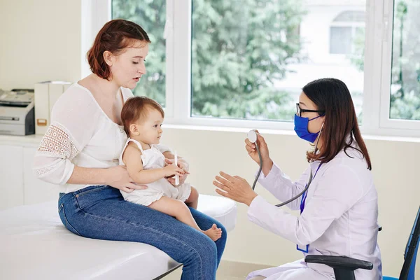 Pediatra Máscara Médica Verificando Batimento Cardíaco Adorável Menina Sentada Voltas — Fotografia de Stock