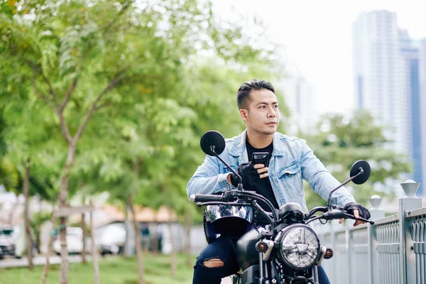 Serious Asiático Hombre Con Teléfono Inteligente Manos Sentado Motocicleta Mirando —  Fotos de Stock
