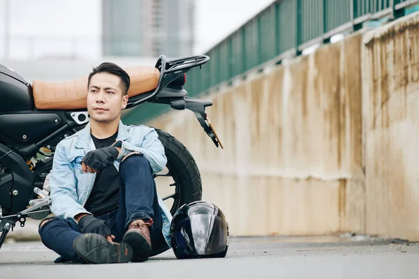 Poważny Przystojny Wietnamczyk Siedzi Ziemi Obok Motocykla Odwraca Wzrok — Zdjęcie stockowe