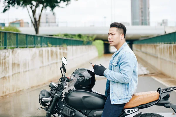 年轻的亚洲摩托车手皱着眉头环顾四周 因为他迷失在陌生的城市里 — 图库照片