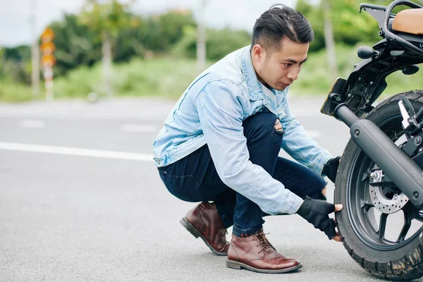Yakışıklı Vietnamlı motosikletçi motoru pompalamak için lastiğini çıkarıyor.