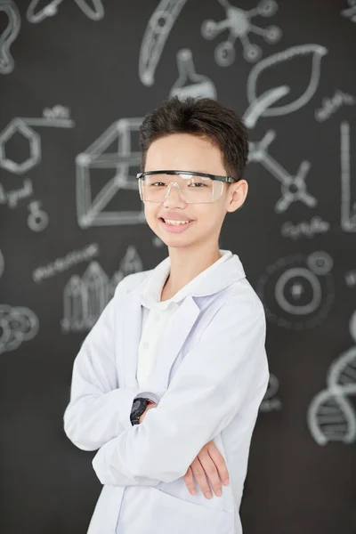 穿着工作服 拿着科学画站在黑板前笑的学童的画像 — 图库照片