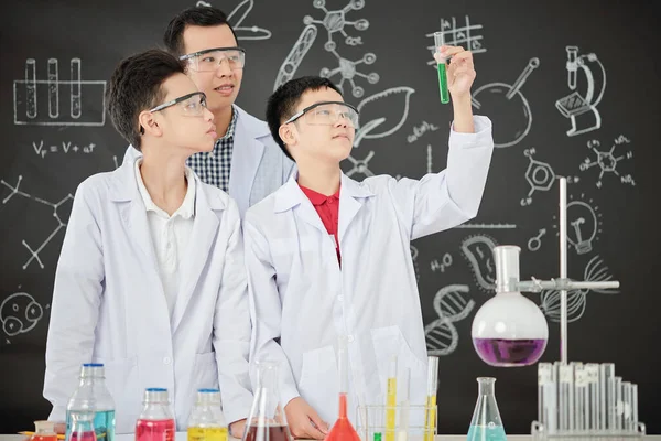 Stolt Asiatisk Skoledreng Viser Reagensglas Med Grøn Væske Til Sin - Stock-foto