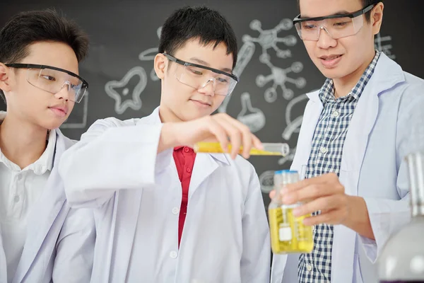 在化学课上 在烧杯里 用护目镜倒试剂微笑的学生在老师手里 — 图库照片