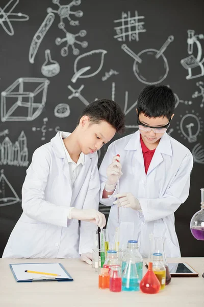 Kimya dersinde çiftler halinde çalışan konsantre Asyalı öğrenciler, reaktörleri karıştırıp not alıyorlar.