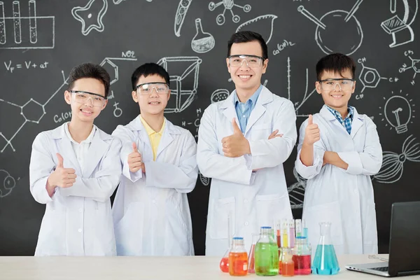 Fröhliche Naturwissenschaftlerin Und Eine Gruppe Schüler Laborkitteln Zeigen Daumen Hoch — Stockfoto