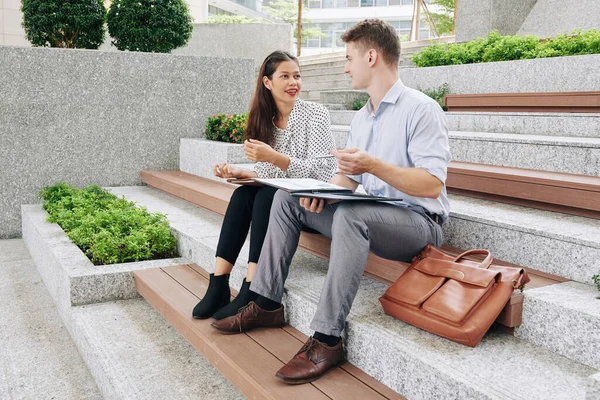 Genç finans yöneticileri açık havada oturup raporları, çizelgeleri ve grafikleri tartışıyor.