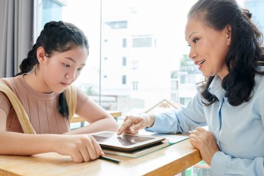 Genç kıza zor konuları anlatırken tablet ekranına işaret eden olgun Asyalı öğretmen
