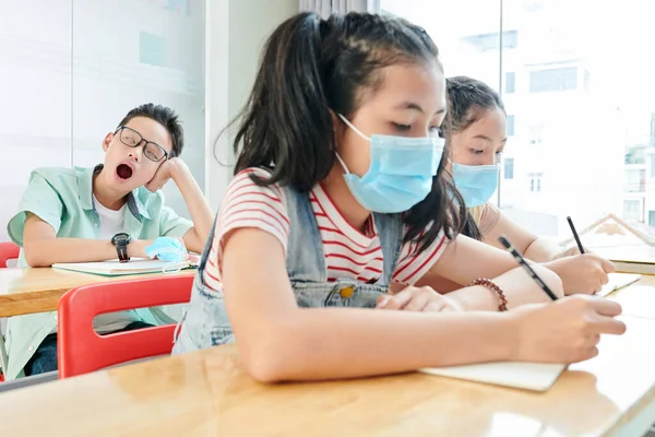 의료용 마스크를 여학생들이 급우가 뒤에서 하품을 — 스톡 사진