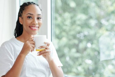 Çekici, gülümseyen Vietnamlı bir kadının portresi. Elinde lezzetli bir sabah kahvesiyle pencerede duruyor.