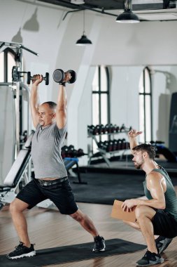 Koç müşteriyi düzeltiyor ve her iki elinde dambıl tutuyor.