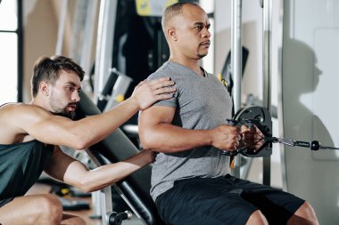Kişisel antrenör müşterisini kontrol ediyor. Spor salonunda sıra makinesinde egzersiz yaparken kendini tutuyor.