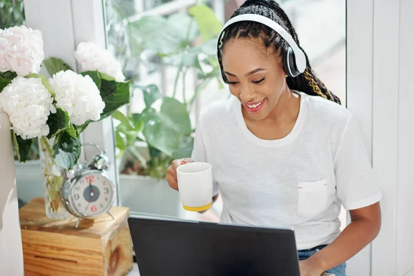 迷人的微笑的年轻黑人女人喝着早上的咖啡 在笔记本电脑上查电子邮件 — 图库照片