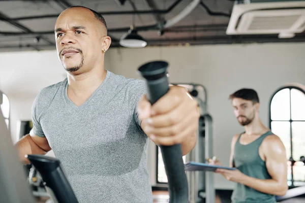 Maduro Sério Homem Andando Elíptico Máquina Ginásio Seu Personal Trainer — Fotografia de Stock