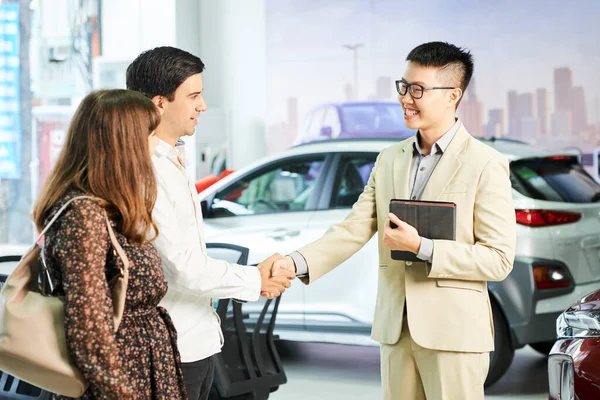 Asian Manager Eyeglasses Smiling Greeting Young Couple Handshake Car Showroom — Stock Photo, Image