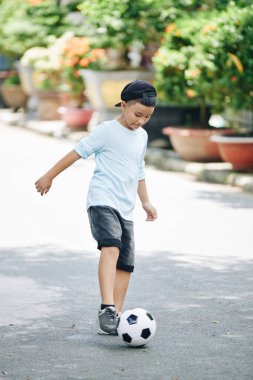 Çocuk yolda tek başına futbol oynuyor ve top sektirmeyi öğreniyor.