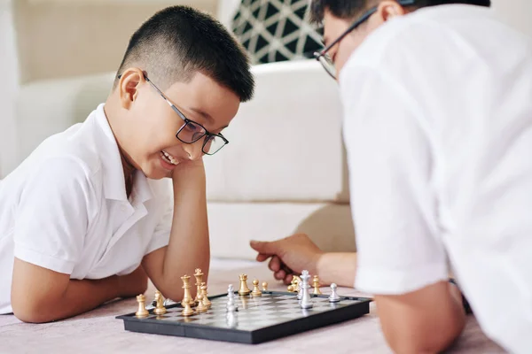 与爸爸下棋时 戴着眼镜的快乐的十几岁前的亚洲男孩在想下一步该怎么走 — 图库照片