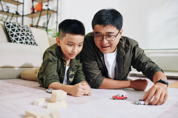 Neşeli çocuk babasıyla oyuncak arabalarla oynarken oturma odasında yerde yatıyorlardı.