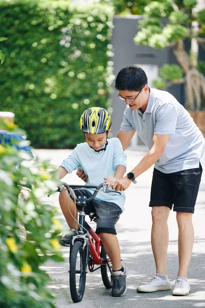 幸せなアジアの男教えPreteen息子でヘルメット乗馬自転車で家の裏庭 — ストック写真