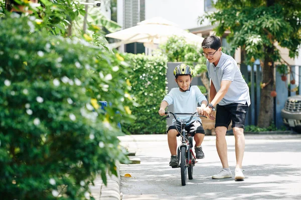 彼の十代の息子が初めて乗っているときに陽気父は自転車のハンドルバーを保持しています — ストック写真