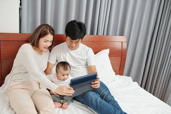 両親と小さな子供見面白い漫画上タブレットコンピュータ上で夜のベッドで休んでいるとき — ストック写真