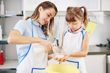 Annesi içine taze soğuk süt dökerken elinde ölçü kavanozu tutan kız.