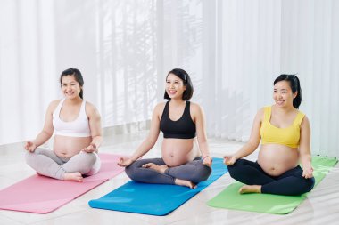 Bir grup neşeli Asyalı hamile kadın sağlık kulübünde yoga yapıyor.