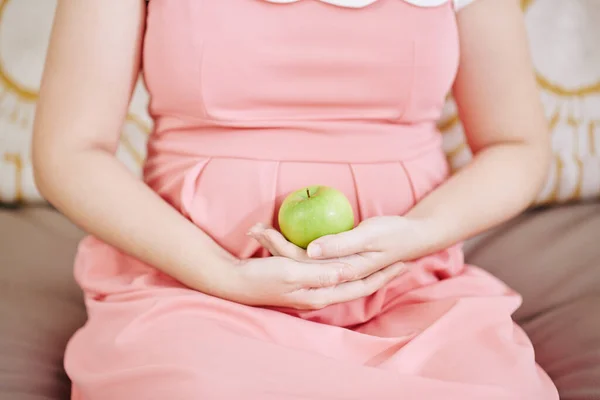 怀孕妇女手拿青苹果坐在沙发上的剪影 — 图库照片