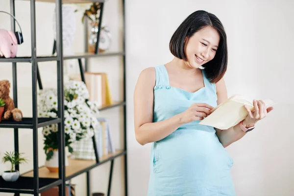 快乐漂亮的年轻越南孕妇阅读有关怀孕和养育子女的有趣书籍 — 图库照片