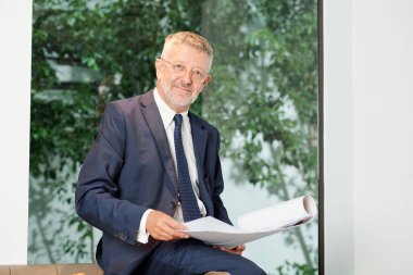 Bina planıyla gülümseyen baş mühendisin portresi kameraya bakıyor.