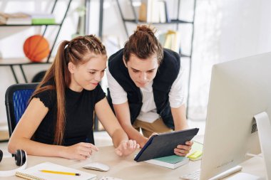 Online bilgisayar bilimleri dersinde kız kardeşine uygulamayı tablet bilgisayarında gösteren genç çocuk.