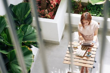 Gülümseyen genç Vietnamlı kadın sabahını kafede geçiriyor ve tablet bilgisayardan haber okuyor.