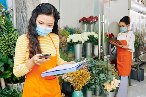 Junge Asiatische Floristin Medizinischer Maske Überprüft Textnachrichten Und Benachrichtigungen Auf — Stockfoto