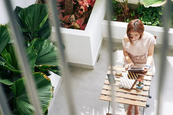 Gülümseyen genç Vietnamlı kadın sabahını kafede geçiriyor ve tablet bilgisayardan haber okuyor.