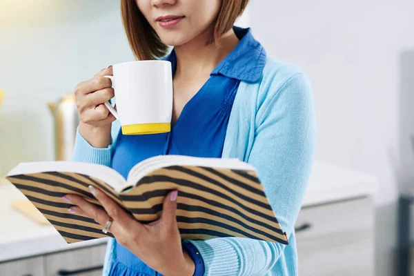 熱いおいしい朝のコーヒーを飲んでいる女性の作物のイメージと面白い小説を読む — ストック写真