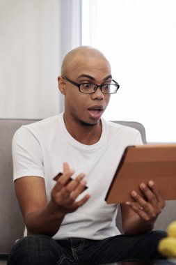 Kredi kartıyla bilgisayar tabletine bakan, faturaları ödeyen ya da alışveriş yapan şaşırmış bir adam.