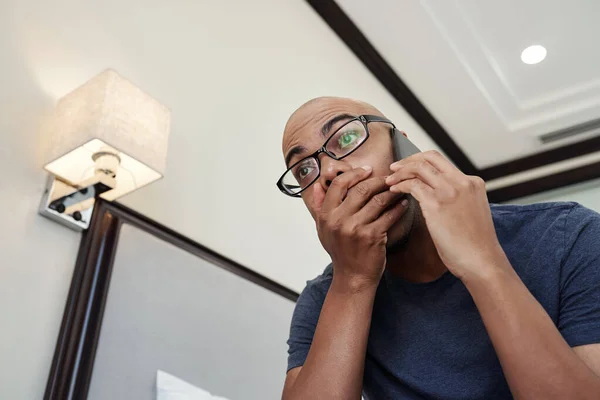Black man receiving shocking news on the phone and covering mouth with hand from excitement