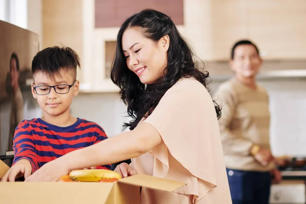 かなり笑顔成熟した女性と彼女の息子は段ボール箱から新鮮な果物や野菜を取って — ストック写真