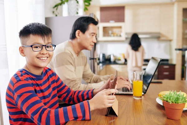 Gülümseyen Asyalı Gözlüklü Çocuk Mutfak Masasında Internetten Ders Çalışıyor Babası — Stok fotoğraf