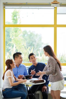 İş adamlarından oluşan bir ekip kafe masasında oturuyor ve iş geliştirmek için yeni yaratıcı fikirler sunan bayan meslektaşlarına bakıyor.