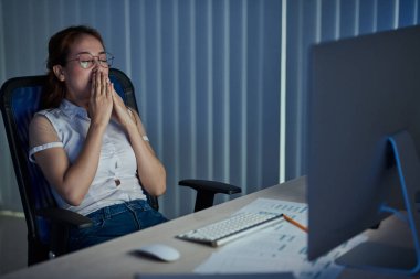 Genç Asyalı UX tasarımcısı bütün gece çalıştıktan sonra yorgun ve uykulu bir şekilde ofis koltuğuna yaslanıyor.