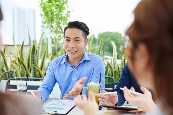 カフェテーブルで同僚との正の若いベトナム人起業家会議 レモネードを飲み 同僚と話す — ストック写真