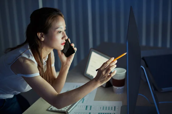 夜遅くまでオフィスに滞在するときに携帯電話のアプリケーションインターフェイスのデザインの詳細を議論するために電話をかける若いアジアのプロジェクトマネージャー — ストック写真