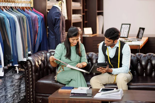 Pretty young Indian woman and tailor choosing clothing item from catalog