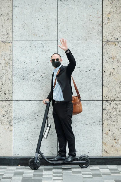 Joven Hombre Negocios Traje Máscara Médica Montando Scooter Saludando Cámara — Foto de Stock