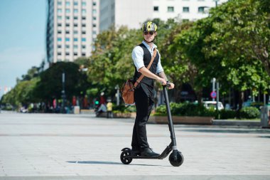 Güneş gözlüklü ve kasklı ciddi bir stil adamı scooter kullanıyor.