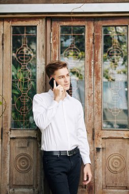Dışarıda dikilirken telefonda konuşan beyaz gömlekli çekici genç adam.