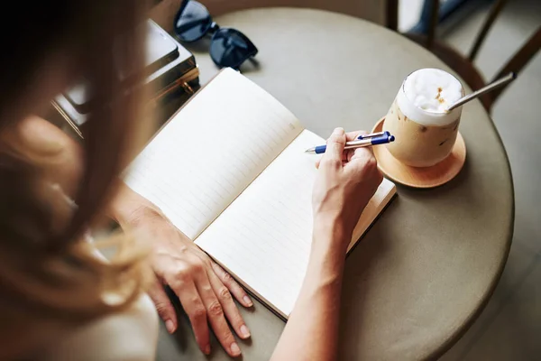 富有创造力的年轻女子在咖啡馆桌边喝咖啡 并在日记中写下自己的想法和想法 — 图库照片