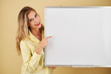 Pozitif genç kadın boş tahtayı gösteriyor ve kameraya gülümsüyor.